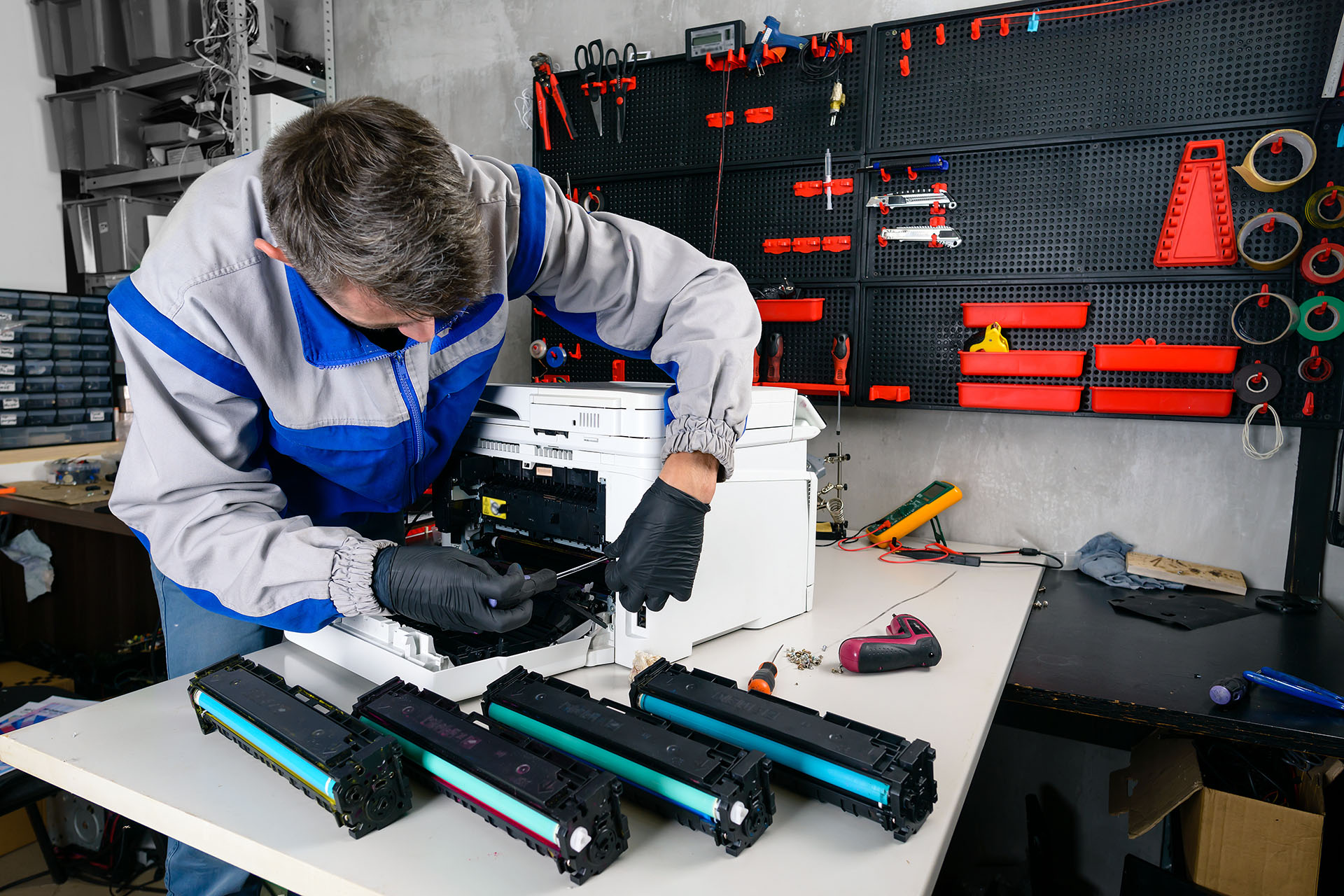 Essential Technical Solutions technician repairing a printer at the workbench, surrounded by toner cartridges and diagnostic tools